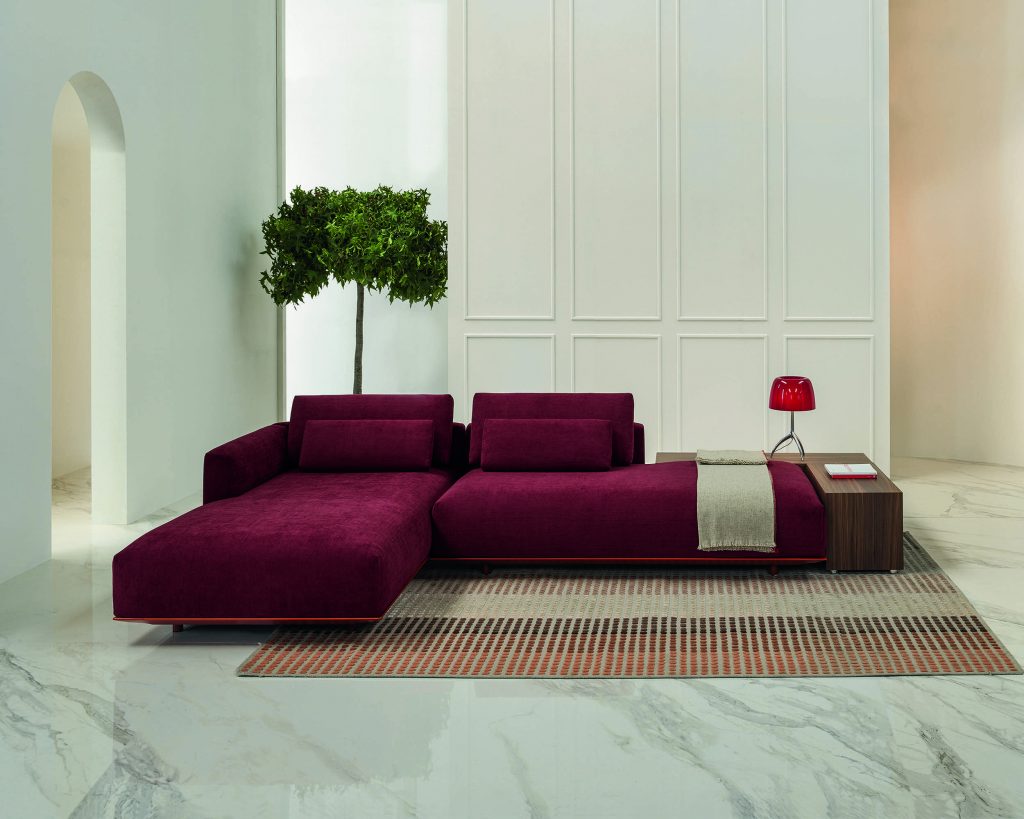 Frontal view of magenta colored Billie on top of a multicolored woven rug with marble flooring and white walls