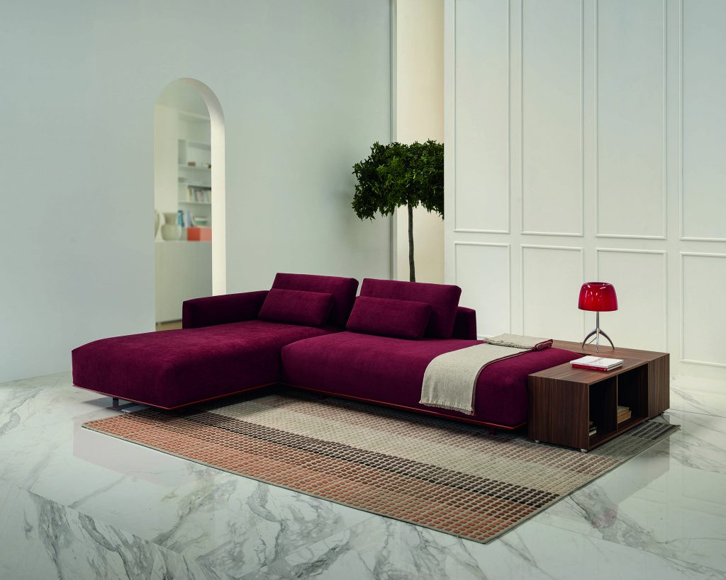 Angled view of magenta colored Billie on top of a multicolored woven rug with marble flooring and white walls