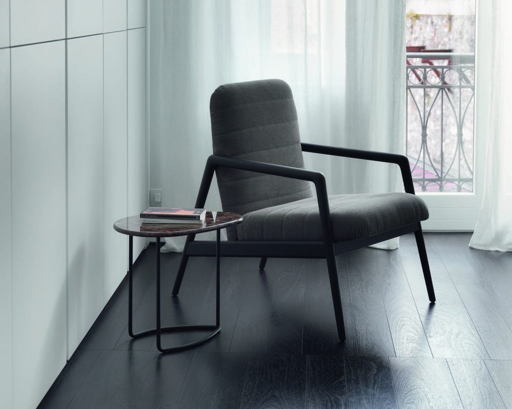 Carnaby in a dark grey color with a small glass table next to it with curtains in the background