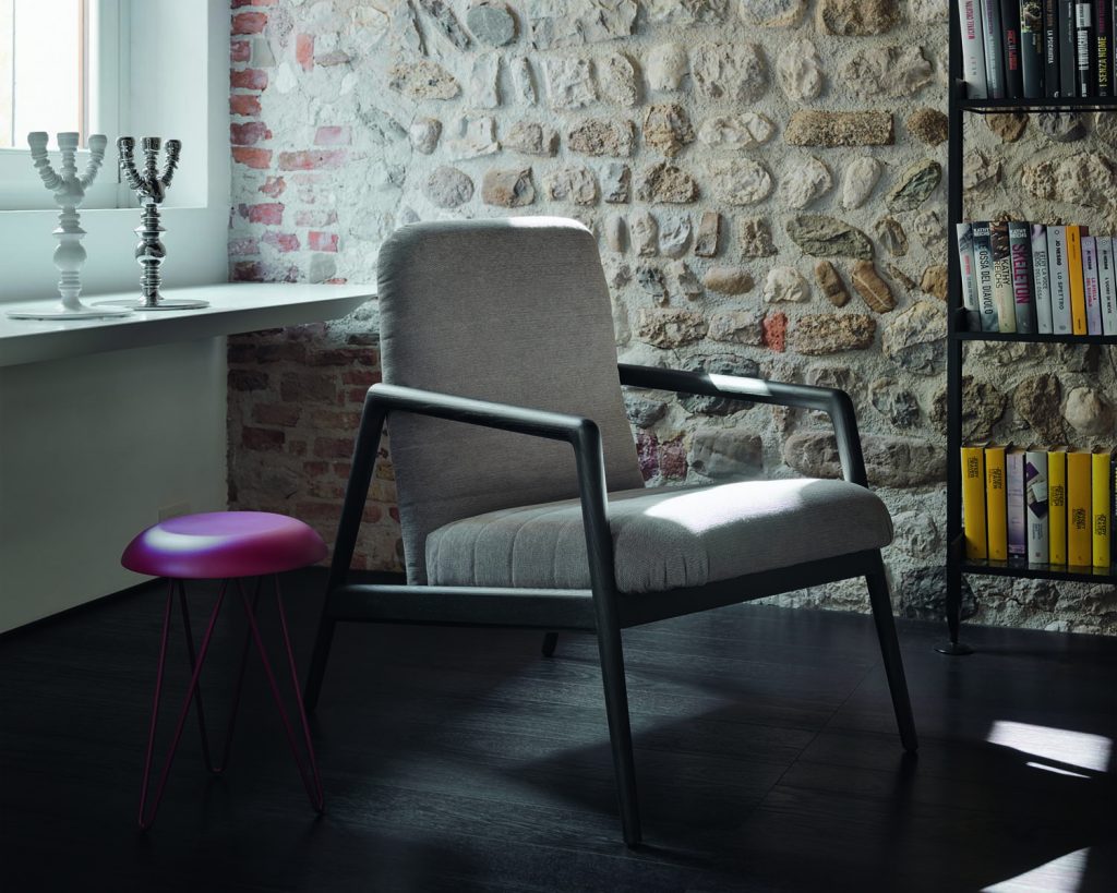 Carnaby chair in a cream color on a dark wooden floor with a window and stoned wall in the background