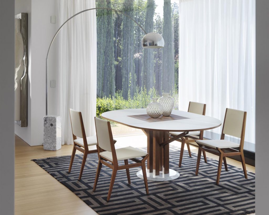 Flower with a white top with white chairs surrounding the table in front of a sunny window