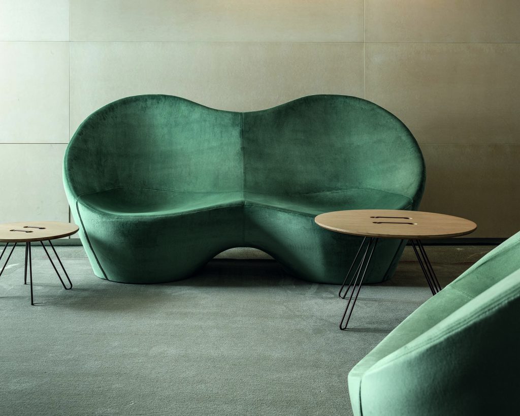 Ouch&Kouch in green combined, a small table in front of it with a cream colored wall background