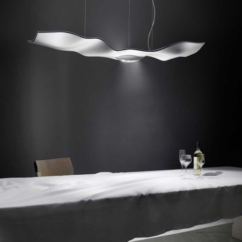 Luce Volante in silver hanging from the ceiling illuminating a table with a black wall in the background