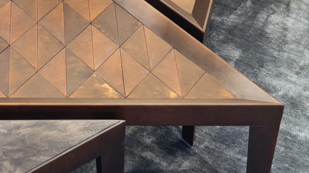 Closeup of a D Code Table triangle shaped top and four legs in brass in a living room.