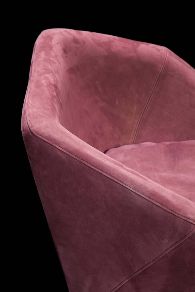 Closeup of Hexagon Armchair upholstered in pink leather and brass finished central leg on a black background.