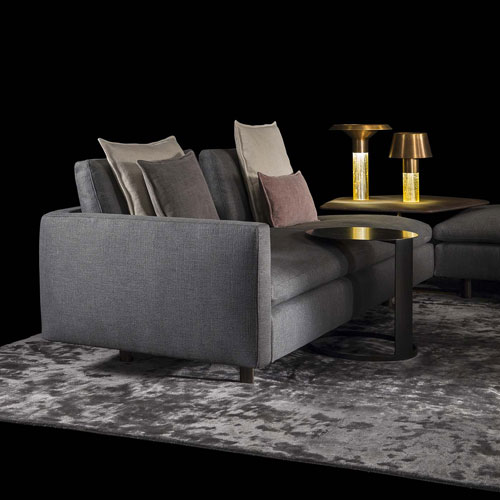 Human Sofa with armrest and backrest upholstered in gray fabric with black brass legs in a living room.