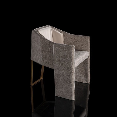 Ketch Chair back leg in brass finish. finish padded seat, back, two legs and arms in gray leather finish, back cushion in gray fabric on a black background.