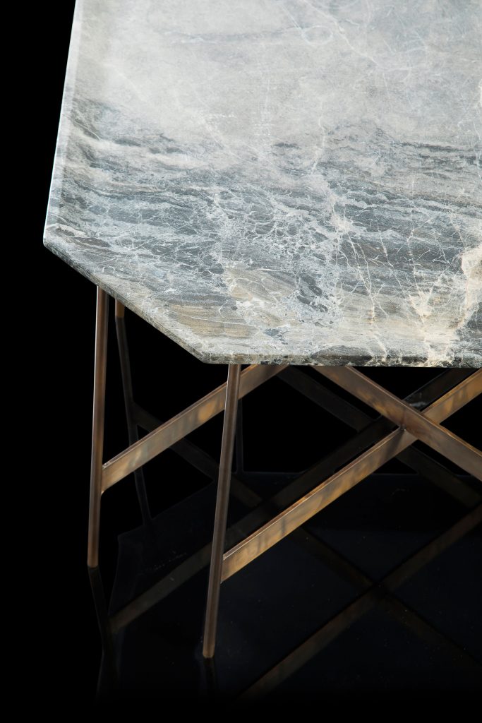 Octagon Table, finish structure and eight legs in burnished brass, top in white and gray stone on a black background.