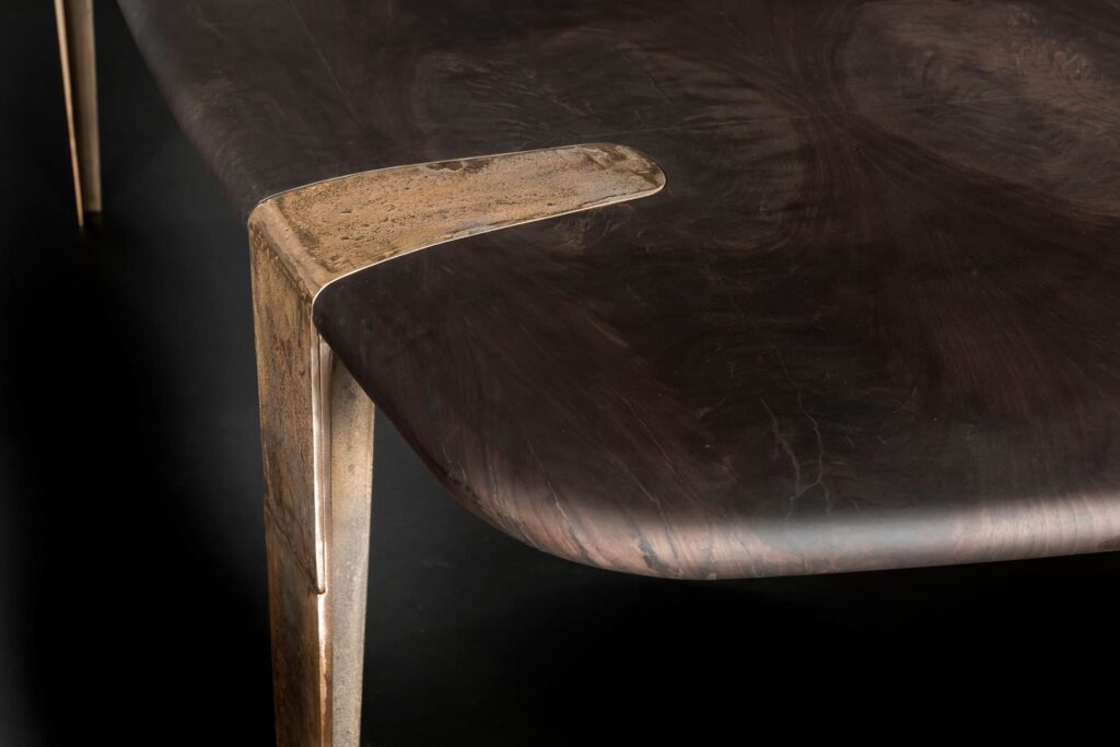 Closeup of Oxymoron Table Structure steel frame with four legs in sandcasting, bronze. Top in natural solidwood on a black background.