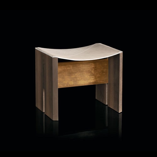 Rio Stool, structure and two legs in natural wood with central crosspiece covered in brass; seat in gray leather on a black background.