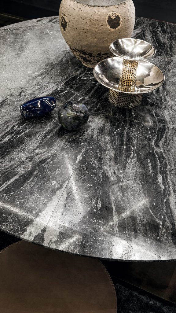 Closeup of a round Shift Table Lounge. Central leg burnished black steel, top in gray and black marble in a dining room.