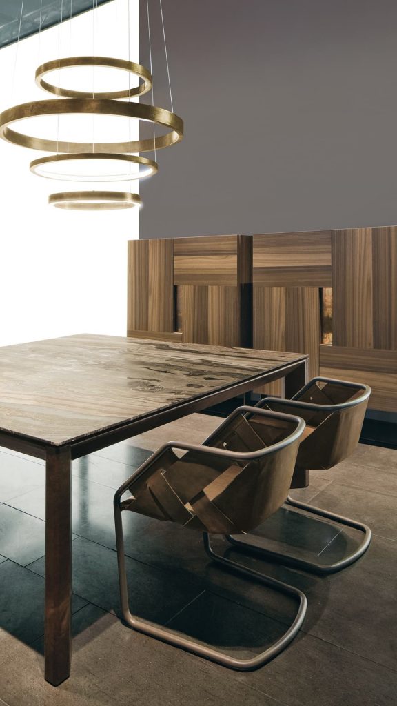 Soprano dining table, structure and four legs in brown wood, top in white, grey, brown and black stone in a dining room.