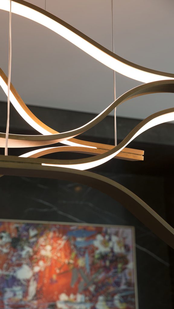 Three led Tape Light with wave shapes creating a dune like pattern using suspension cables. White light and silver structure color on a ceiling.