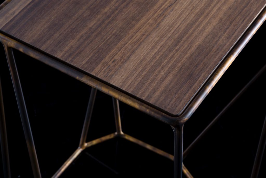 Closeup of W Table, structure in rod metal color bronze, diamond like shape. Top in natual wood on a black background.