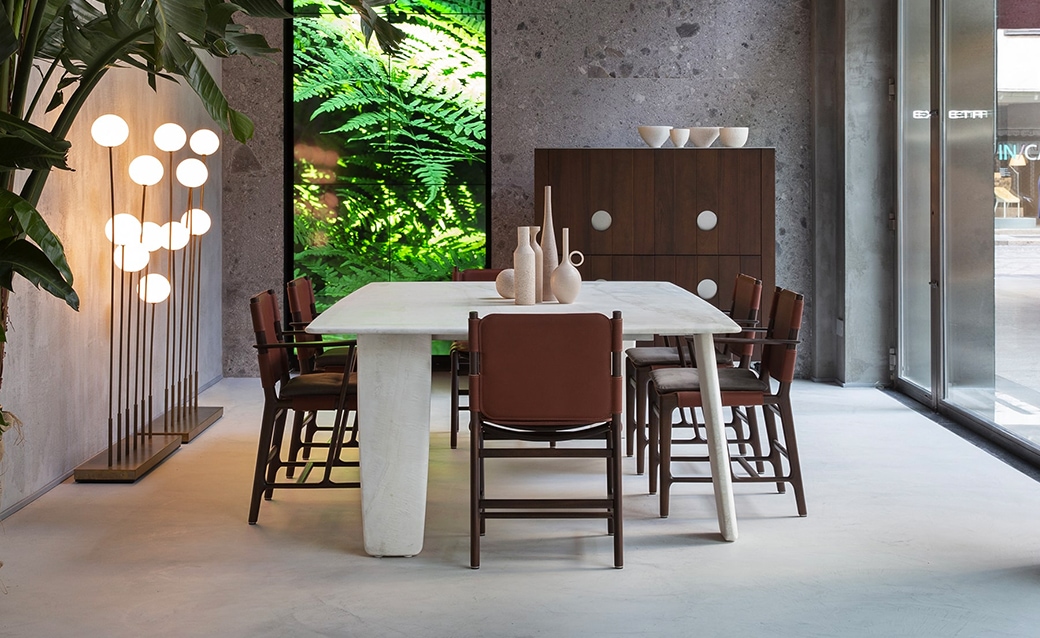 Modern dining area with a concrete table, wooden chairs with leather seats, and a green vertical garden in the background