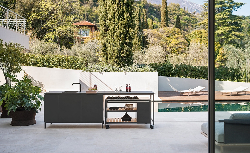 Modern outdoor kitchen with a sleek black countertop and stainless steel elements, set against a scenic hillside backdrop