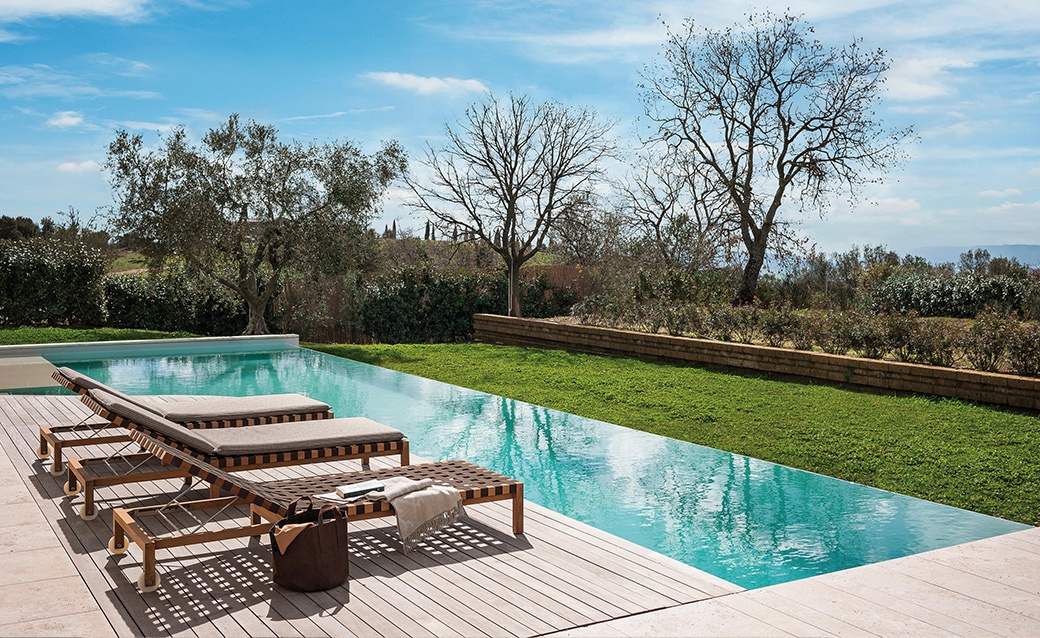 Luxury outdoor poolside setting with wooden lounge chairs and a scenic landscape
