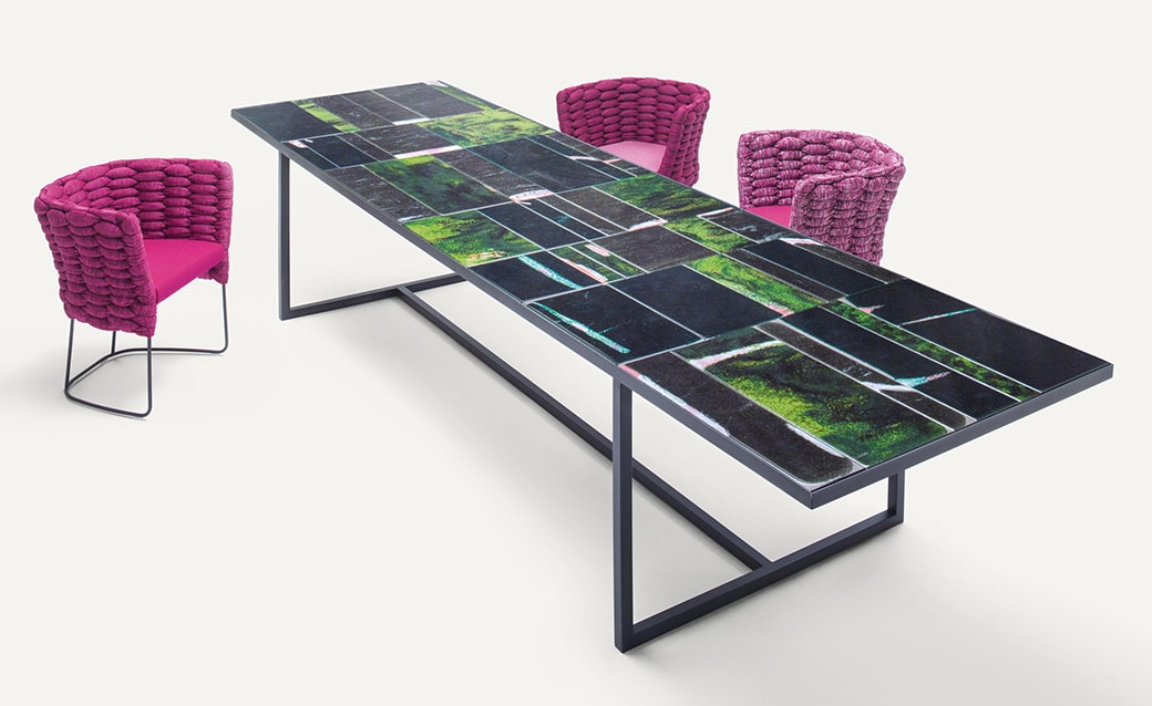 Sciara table with a striking glass surface featuring a vibrant abstract design, paired with bold pink woven chairs