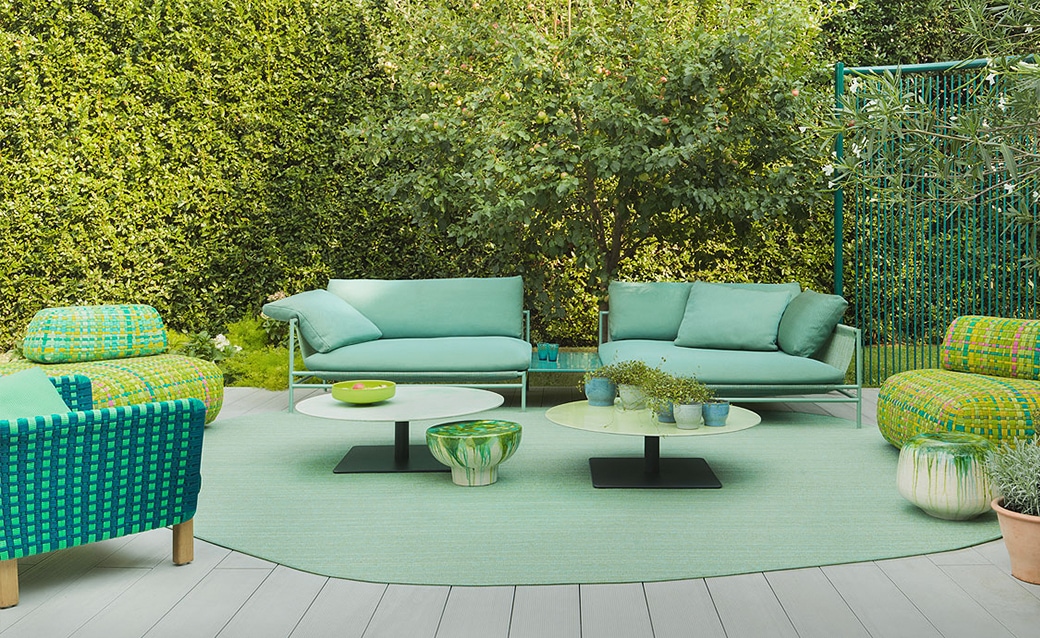 Outdoor seating arrangement in vibrant mint green with matching coffee tables and lush greenery in the background