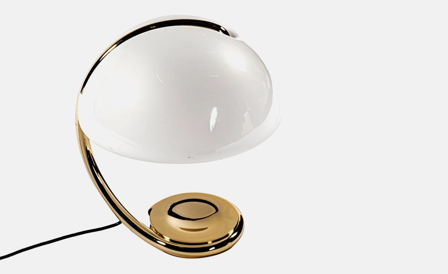 A sleek and modern table lamp featuring a curved brass base and a white glass dome shade, offering a stylish blend of vintage and contemporary design