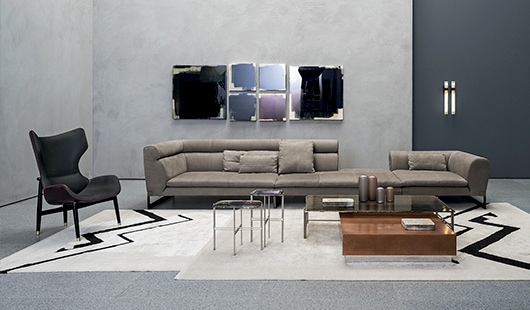 Viktor – A contemporary sofa with tufted upholstery and a sleek metal frame, set against a minimalist concrete wall with reflective artwork, complemented by modern accent tables