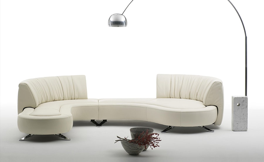 A contemporary cream-colored sectional sofa with a flowing, organic shape, vertical channel tufting on the backrests, and black legs, styled with a modern floor lamp and minimalist decor