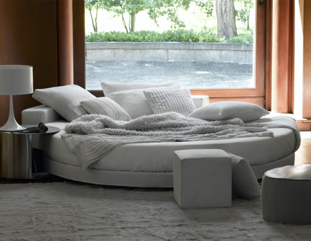 White bed in the shape of a circle with a black wooden backrest on a room
