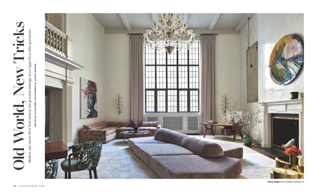 A spacious living room with high ceilings, a large grid-pattern window, and an elegant chandelier, featuring a modern, low-profile sofa and a mix of contemporary and classic furniture pieces