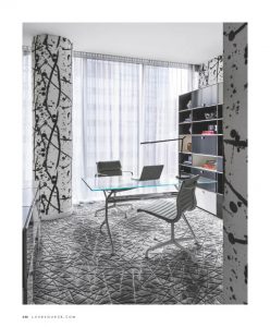 Modern home office with a glass desk, sleek chair, and bold patterned columns, complemented by floor-to-ceiling curtains and a contemporary bookshelf.