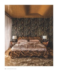 This image showcases a luxurious bedroom with a bold nature-inspired accent wall, a richly patterned bedspread, and matching bedside tables with elegant lamps, creating a warm and opulent atmosphere