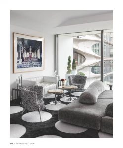 A modern living room with sleek gray furniture, round white tables, and floor-to-ceiling windows offering a view of contemporary architecture.