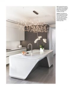 A sleek, modern kitchen featuring a sculptural white island with an angular design, complemented by minimalist cabinetry and a statement chandelier adorned with delicate glass orbs.