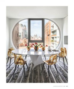 A contemporary dining room featuring a round table surrounded by elegant golden chairs, set against a striking circular window framing a cityscape view.