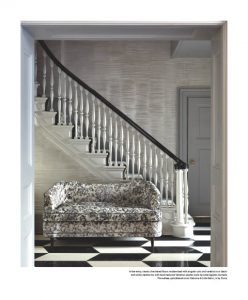 A stylish interior featuring a black and white checkered floor, a grand staircase with a dark wooden handrail, and an elegant patterned sofa placed against the wall beneath the stairs