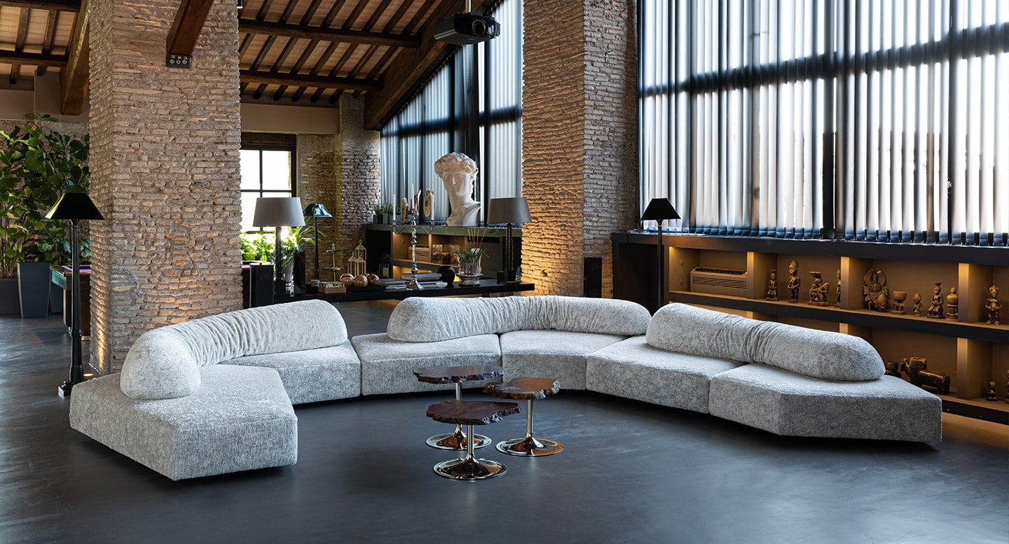 Modern loft with a spacious curved sectional sofa, high ceilings, and industrial-style windows.