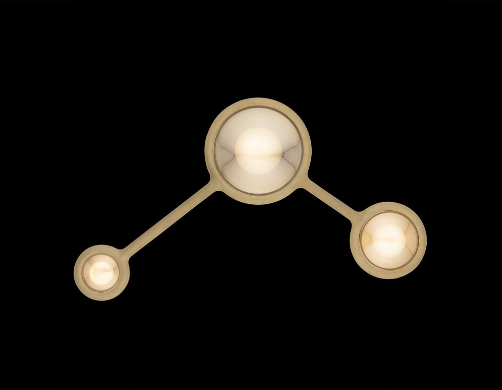 ceiling lamp made of metal by hand in the shape of three connected spheres in a gold and white tone for its LED lighting in a black background