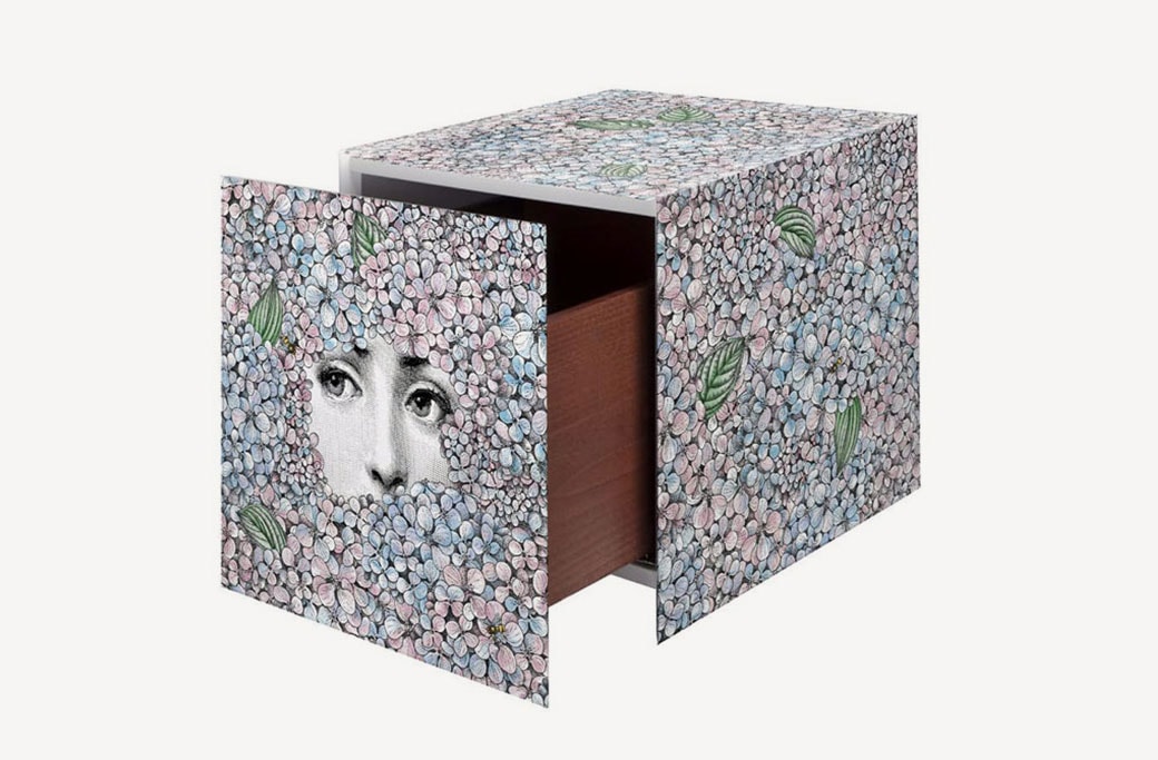 A cube-shaped storage unit featuring a mosaic-like pattern with a surrealist face peeking through, combining artistic expression with functional design