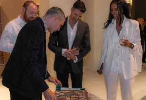 A group of elegantly dressed individuals gathers around a table, engaged in a refined discussion while admiring intricate design details