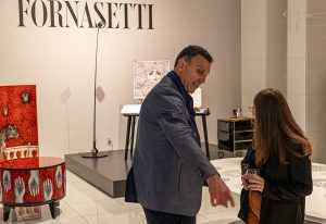 A distinguished gentleman gestures as he converses with a guest in an elegant showroom featuring Piero Fornasetti
