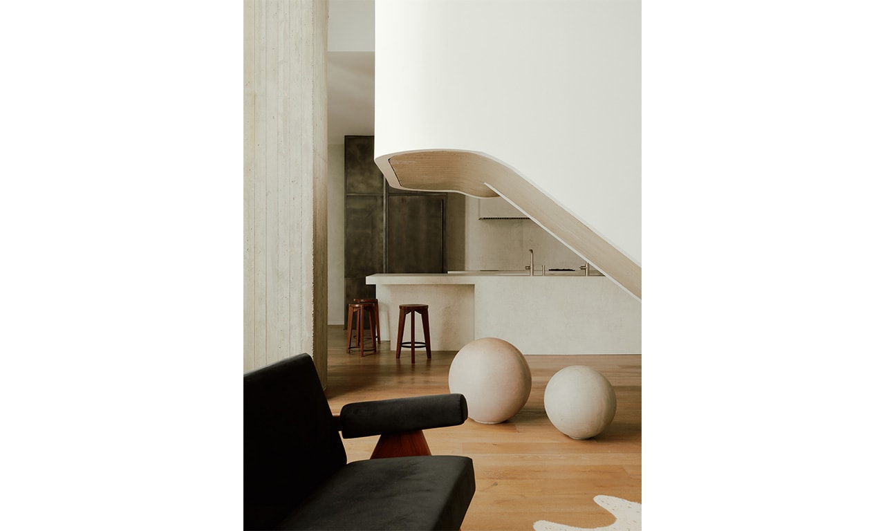 A modern interior featuring a sculptural staircase with smooth curves, contrasted by dark seating and spherical decor elements on warm wooden flooring