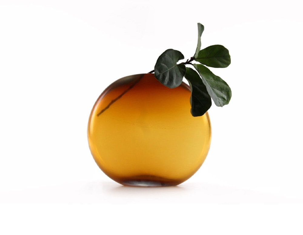 circular glass sculpture in a gradient orange tone with a hole at the top that serves as a vase.