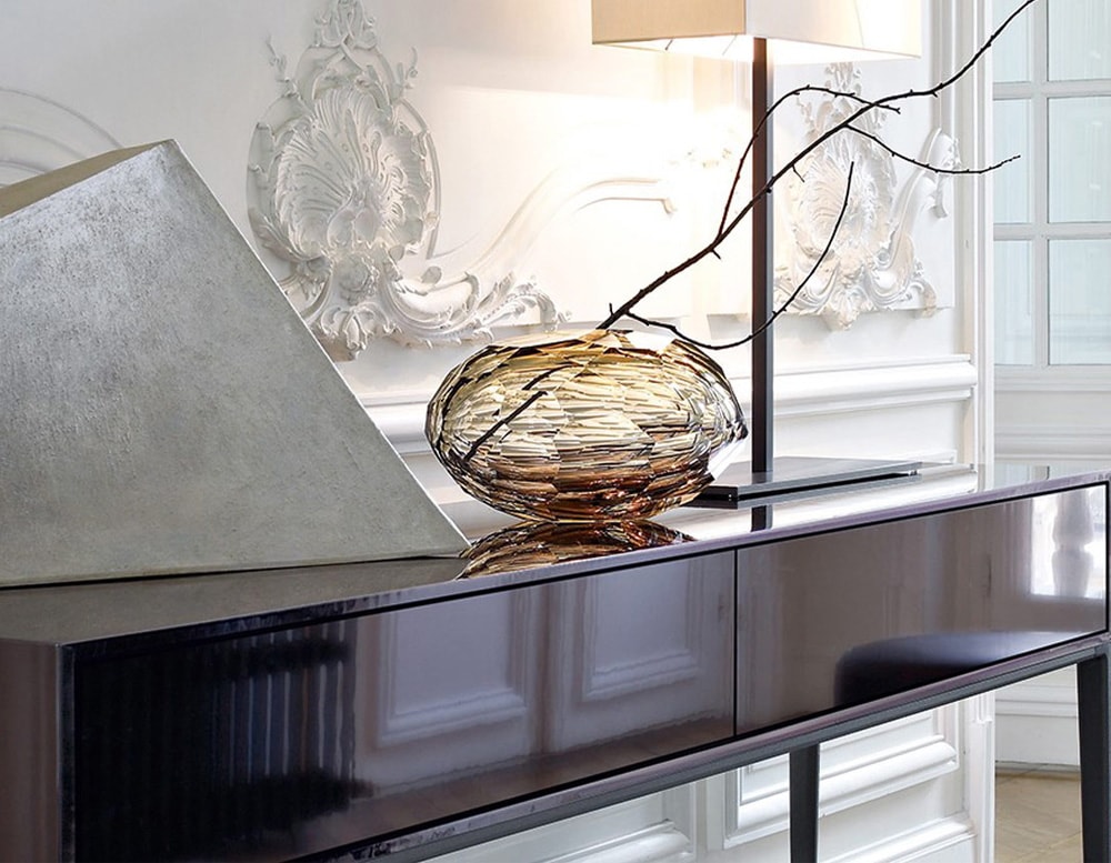 Shiny golden glass sculpture with an oval shape and pentagon-shaped finishes.