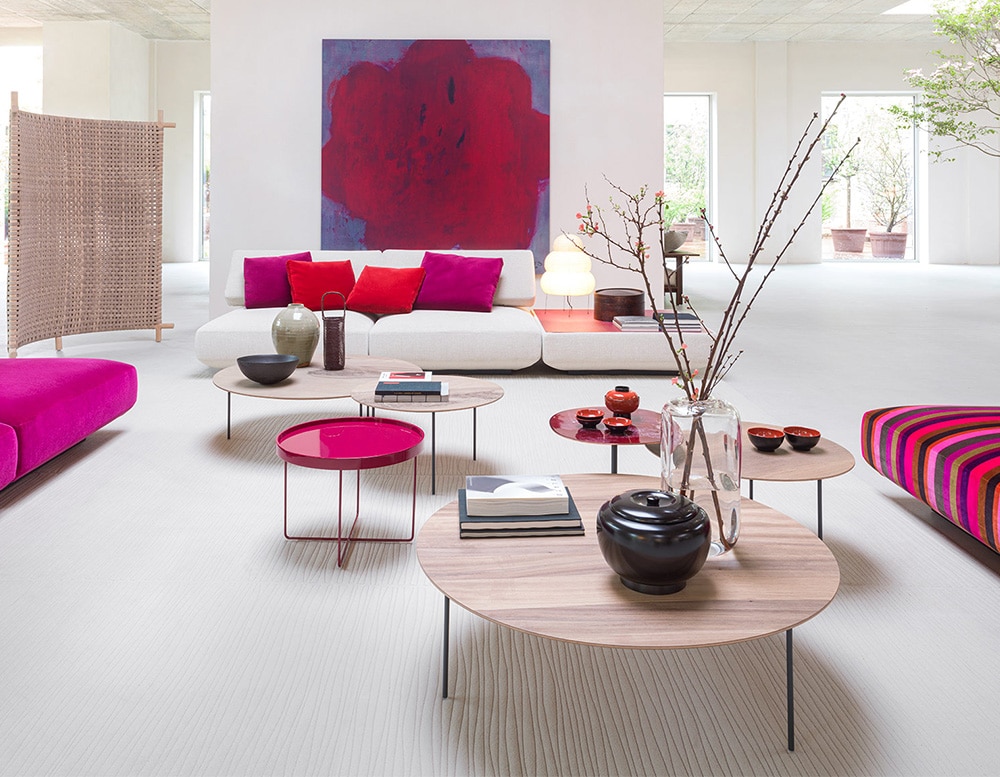 four side tables with multilayer wooden top and matte black varnished stainless steel rod base in a room next to white and fuchsia sofas