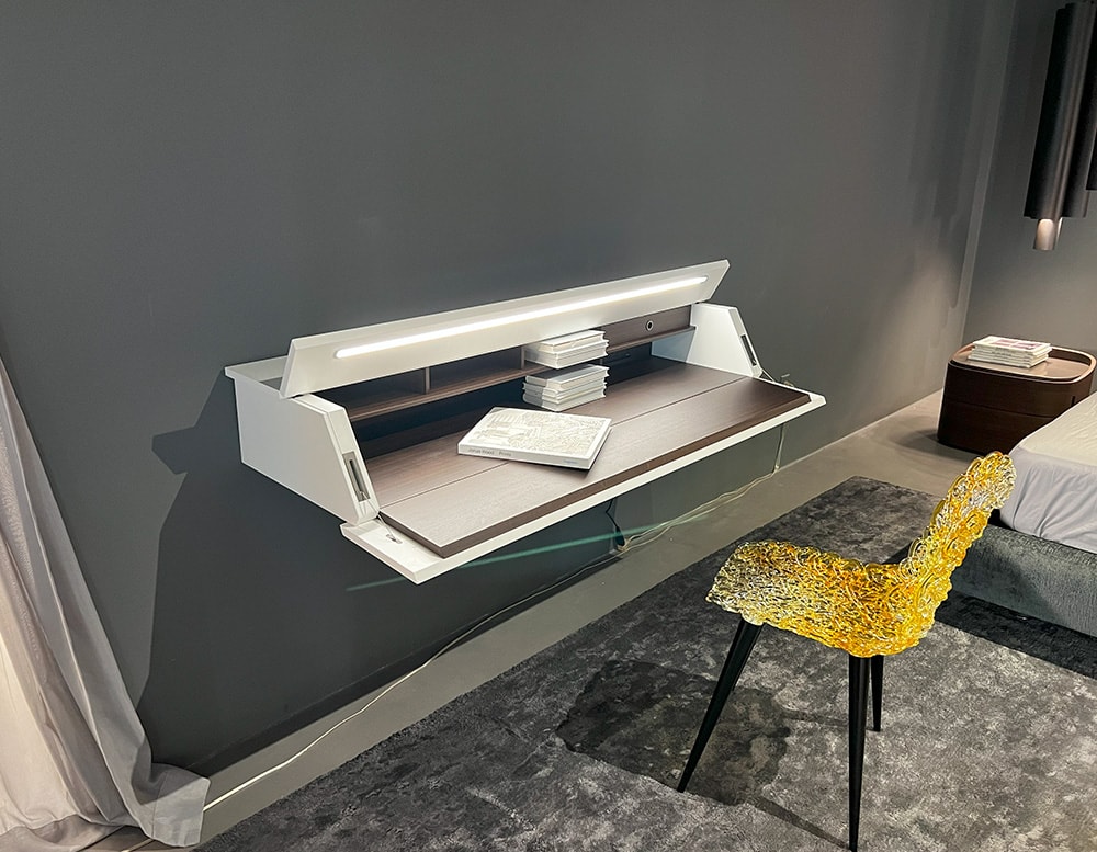 Side view of a writing-desk with a brown wood front panel turning into a handy writing table with a built-in desk light and a white matte color lacquered door and top in a wall