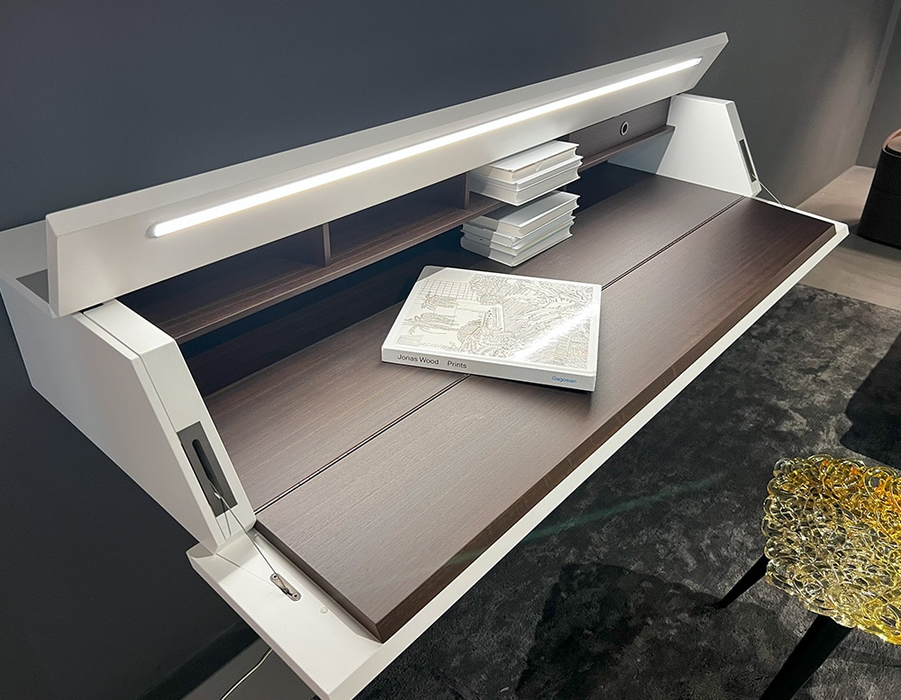 Side view of a writing-desk with a brown wood front panel turning into a handy writing table with a built-in desk light and a white matte color lacquered door and top