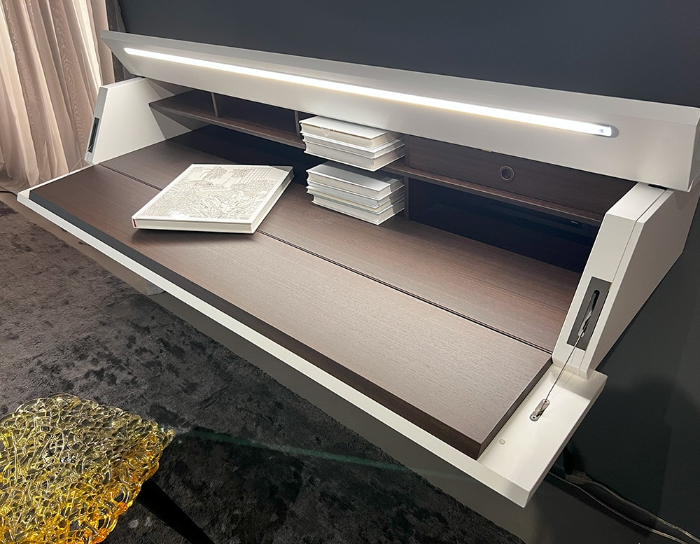 Side view of a writing-desk with a brown wood front panel turning into a handy writing table with a built-in desk light and a white matte color lacquered door and top