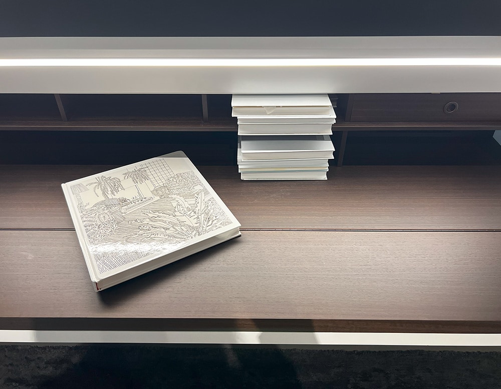 detail view of a writing-desk with a brown wood front panel turning into a handy writing table with a built-in desk light and a white matte color lacquered door and top