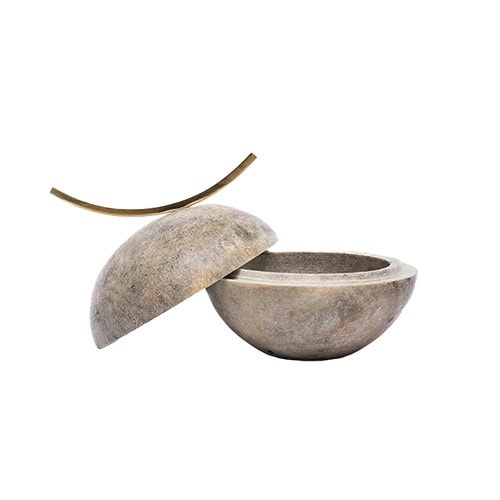A sculptural lidded bowl in natural stone with a smooth finish and organic form, featuring a half sphere lid and a sleek curved metal accent for a refined decorative touch.