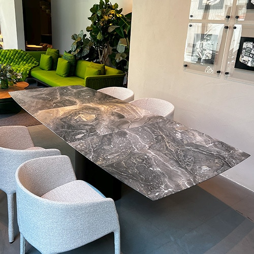 View from above of an extendable dining table boat-shaped made of natural stone with a lifting mechanism for an integrated center-leaf made of natural stone. Top in Black Marble Leathered Stone with a base with castor dark bronze.