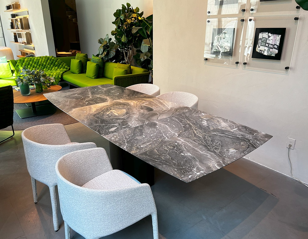 Side view of an extensible dining table, boat-shaped, made of natural stone with lifting mechanism for an integrated center-leaf made of natural stone. The integrated lifting mechanism allows the interior central leaf to be raised once the two halves of the table top have been pulled apart. An ingenious technique makes the extension a procedure of miraculous ease. Top in Black Marble Leathered Stone. Base with Castors Dark Bronze